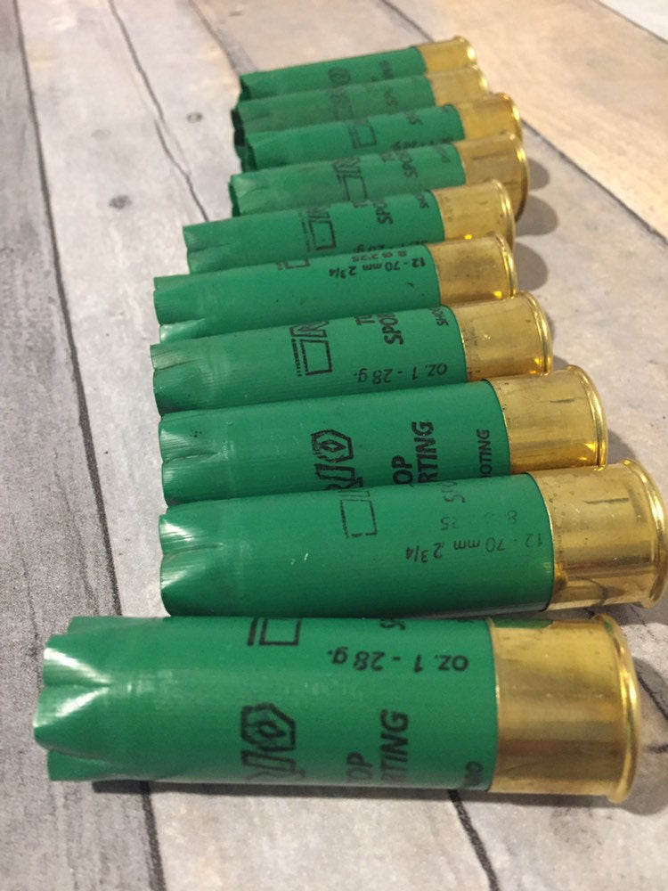Row of empty green 12 gauge RIO Top Sporting shotgun shells with brass bases lying on a wood deck