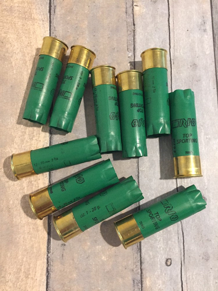 10 empty green 12 gauge RIO Top Sporting shotgun shells with brass bases scattered on a wood deck