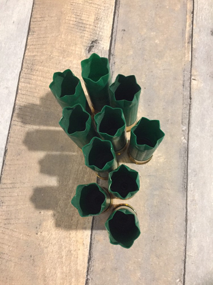 9 empty green 12 gauge shotgun shells with crimped open ends viewed from above showing hollow interiors on a wood deck