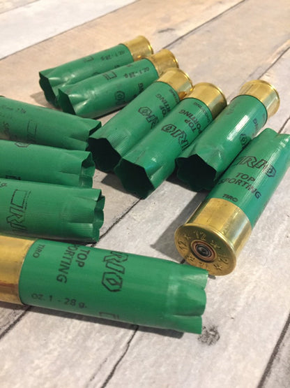 9 empty green 12 gauge RIO Top Sporting shotgun shells with brass bases arranged in a cluster on a wood deck