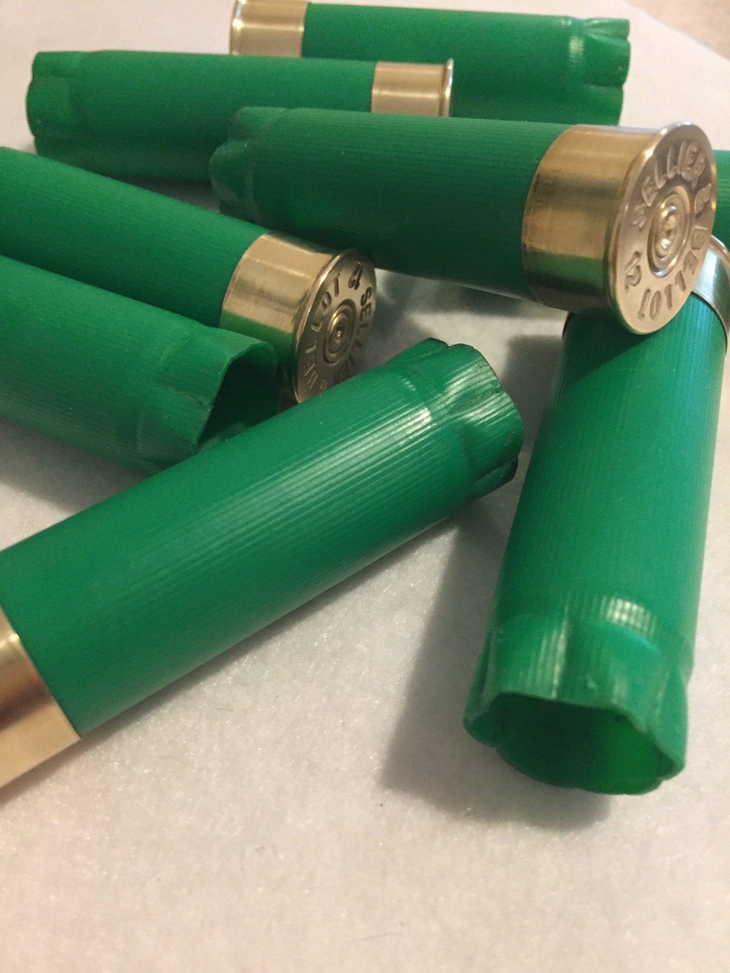 8 green shotgun shells lying together showing gold brass heads with Sellier and Bellot headstamp text