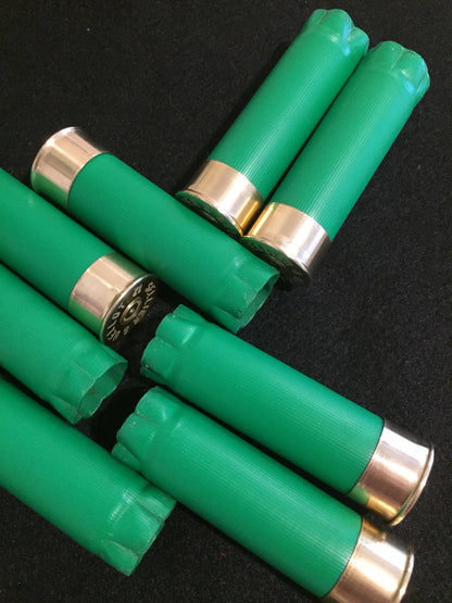 8 green shotgun shells crossed over each other on a dark surface showing gold brass heads