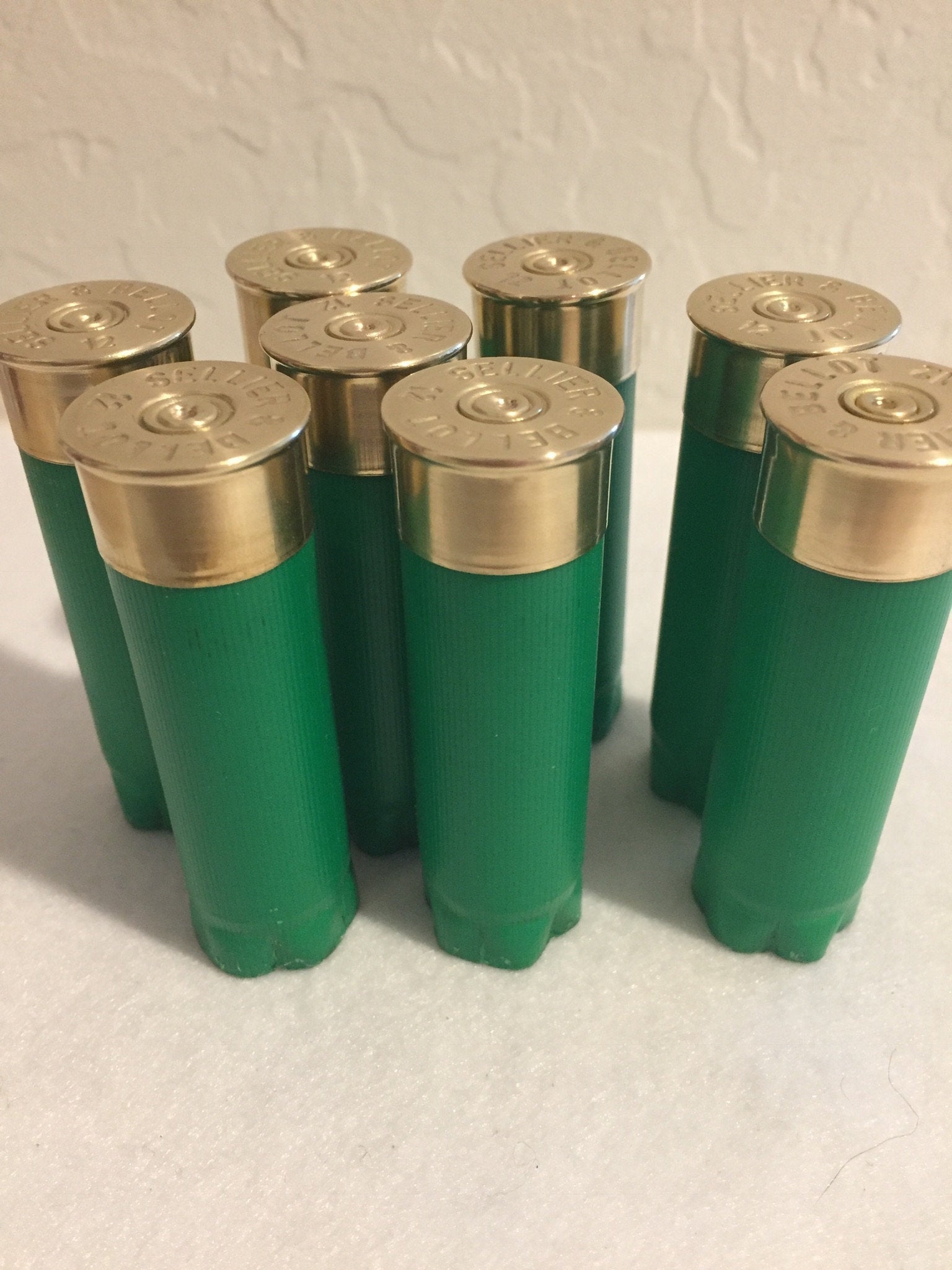 8 green Sellier and Bellot 12 gauge shotgun shells standing upright with gold brass heads against a white wall