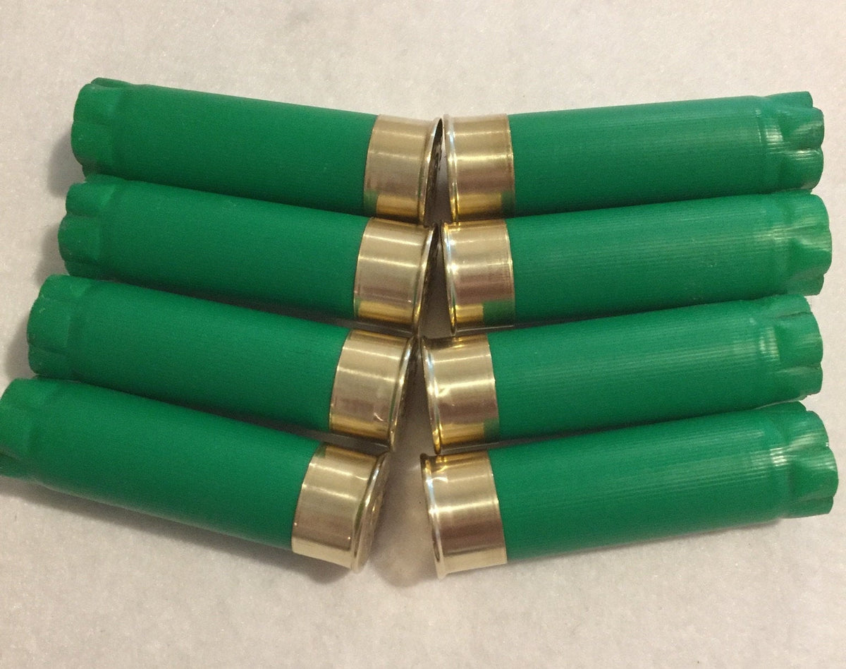 8 green shotgun shells crossed together showing gold brass heads on a white surface