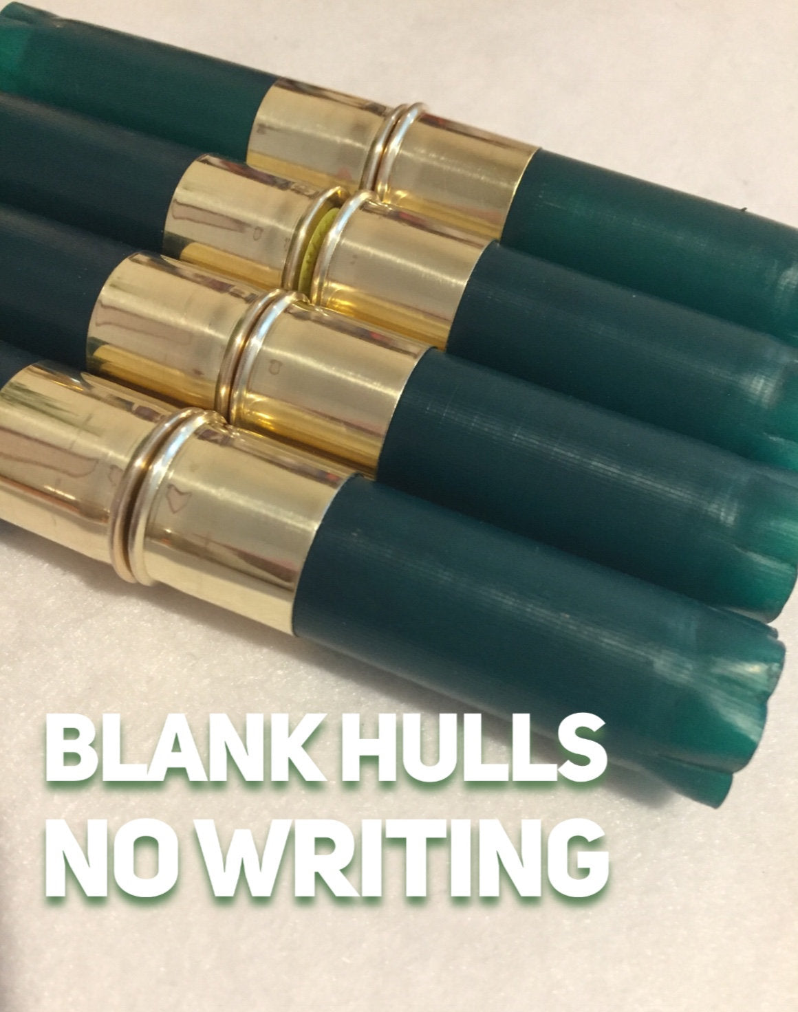 Four green shotgun shells with gold brass bases stacked closely together with text overlay blank hulls no writing.