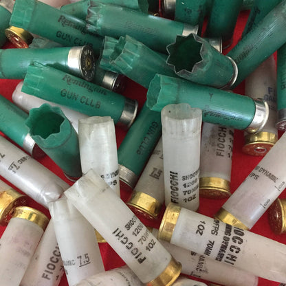 Pile of green and translucent 12 gauge shotgun shell hulls with open crimped mouths on a red background