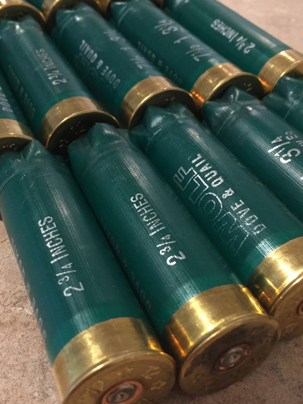 Green shotgun shells with brass bases lying in rows printed "2¾ Inches" and "Wolf Dove & Quail"