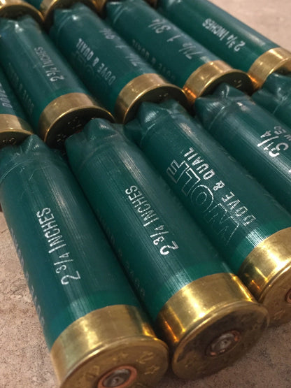 Green shotgun shells with brass bases lying in rows printed "2¾ Inches" and "Wolf Dove & Quail"