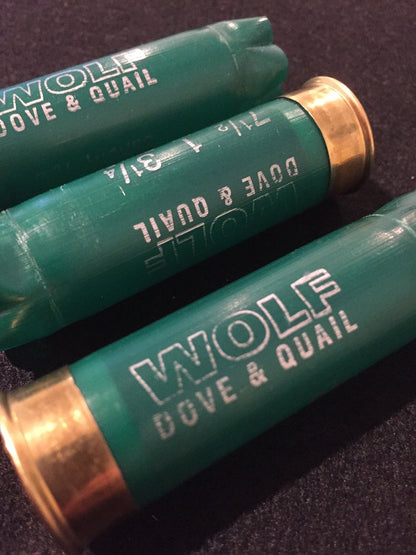 3 green shotgun shells with brass bases lying at angles printed "Wolf Dove & Quail" and "7½ 1 3¼"