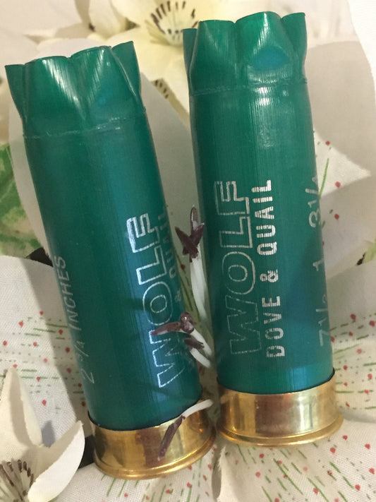 2 green shotgun shells with brass bases standing upright printed "Wolf Dove & Quail" among white flowers