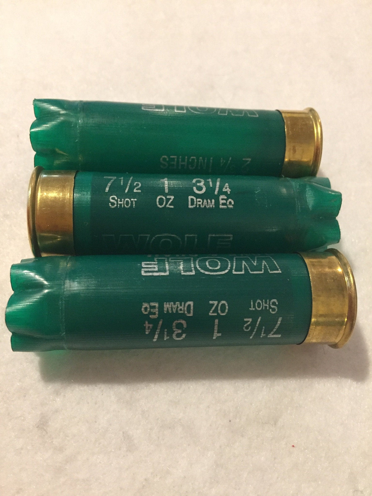 3 green shotgun shells with brass bases lying upside down printed "Wolf", "7½ 1 3¼", "Shot Oz Dram Eq"