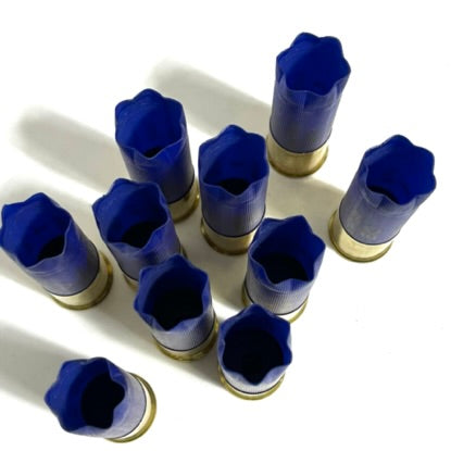 A cluster of nine blue empty 12ga shotgun shells standing upright on a white surface showing 6 star crimp.