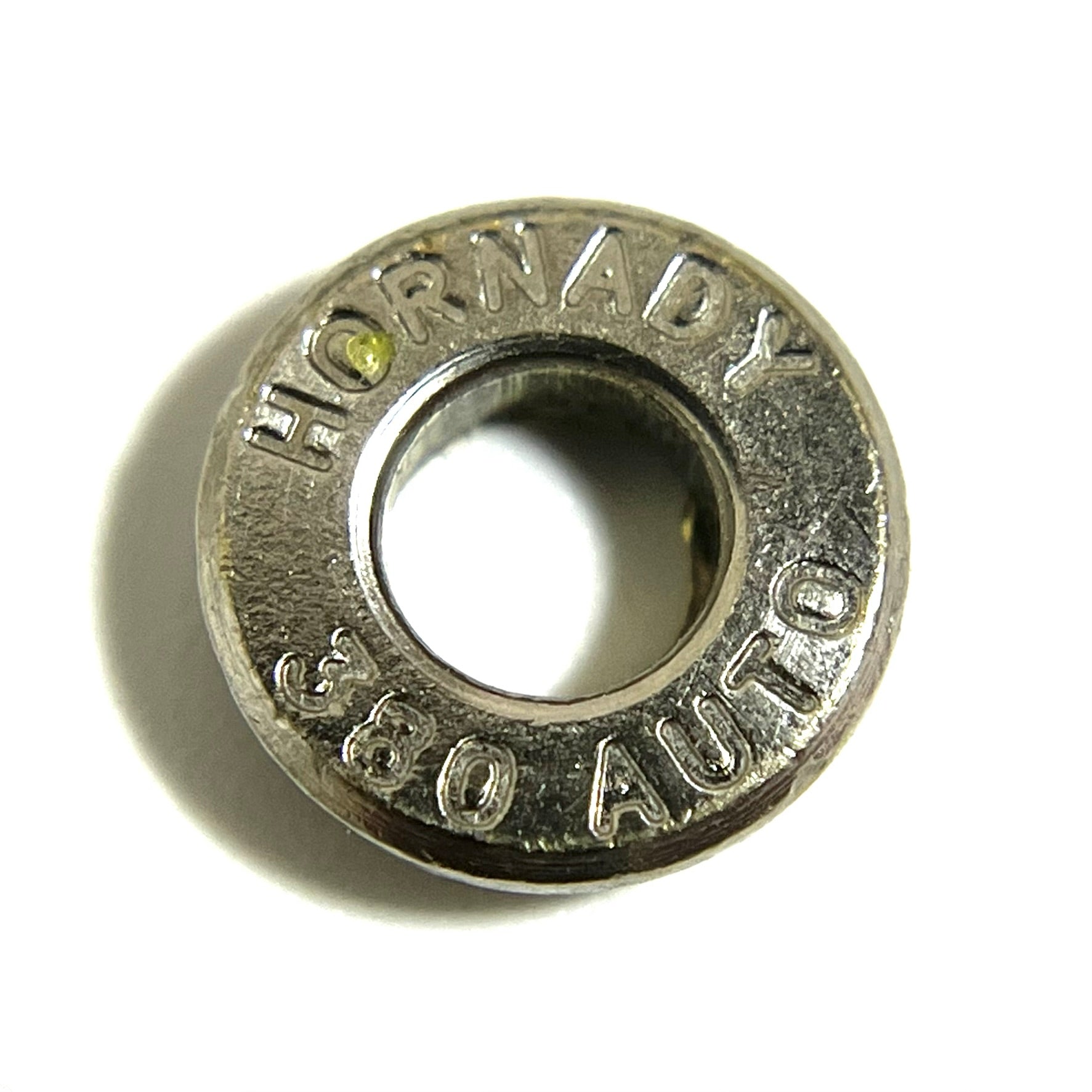 Close-up of a single nickel 380 Auto Hornady bullet slice on white with a deprimed open hole and readable headstamp text.