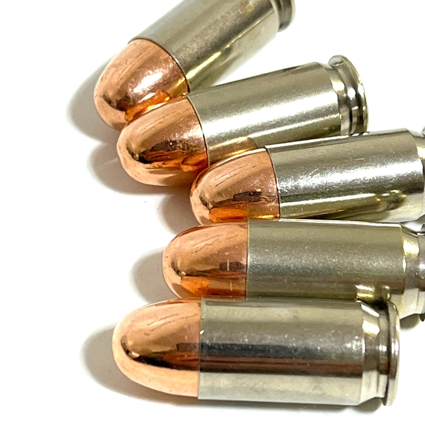 A close up view of five nickel 45 ACP dummy rounds with copper round nose bullets stacked on a white background.