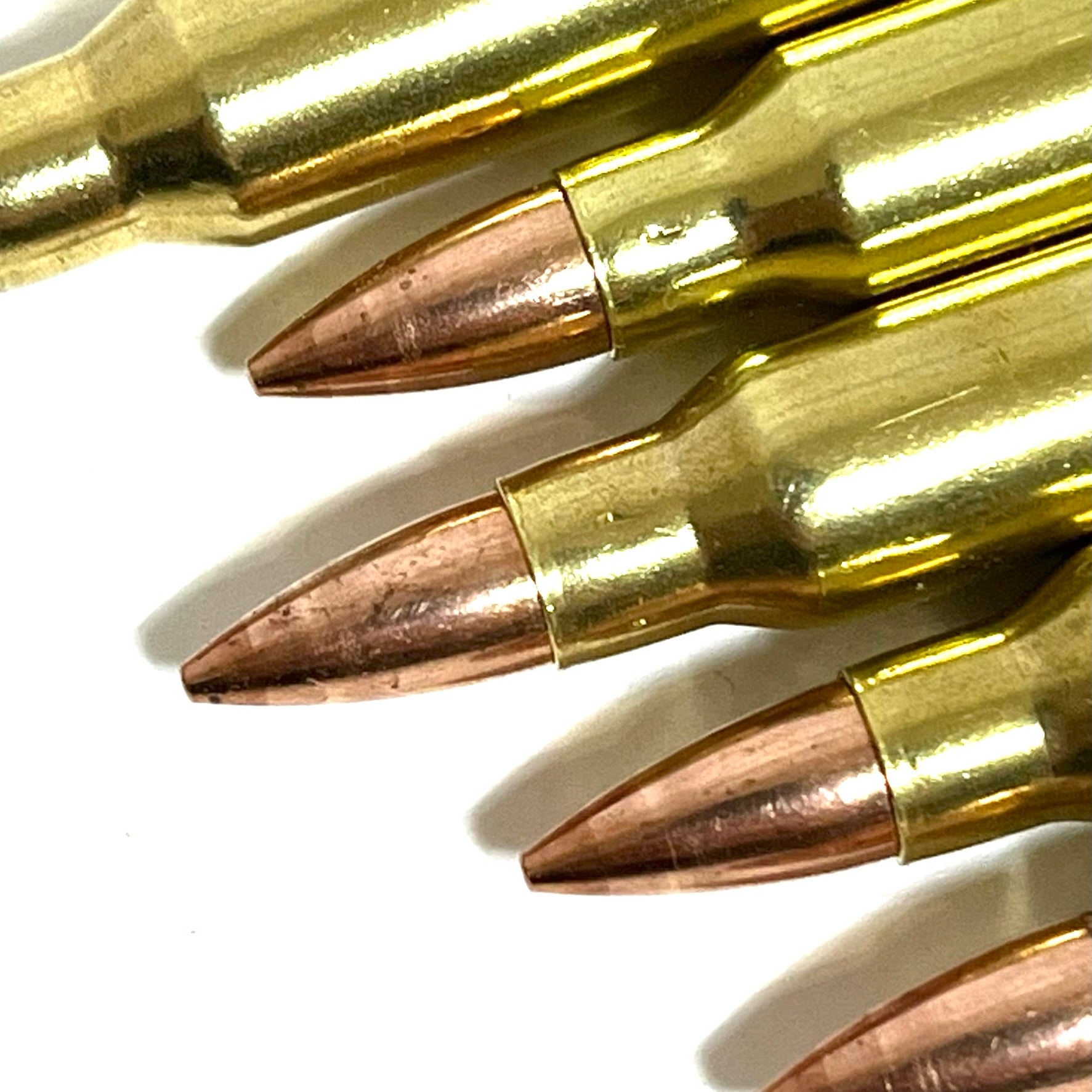 A detailed close-up shot of the copper tips of five brass inert rifle fake cartridges stacked closely together.