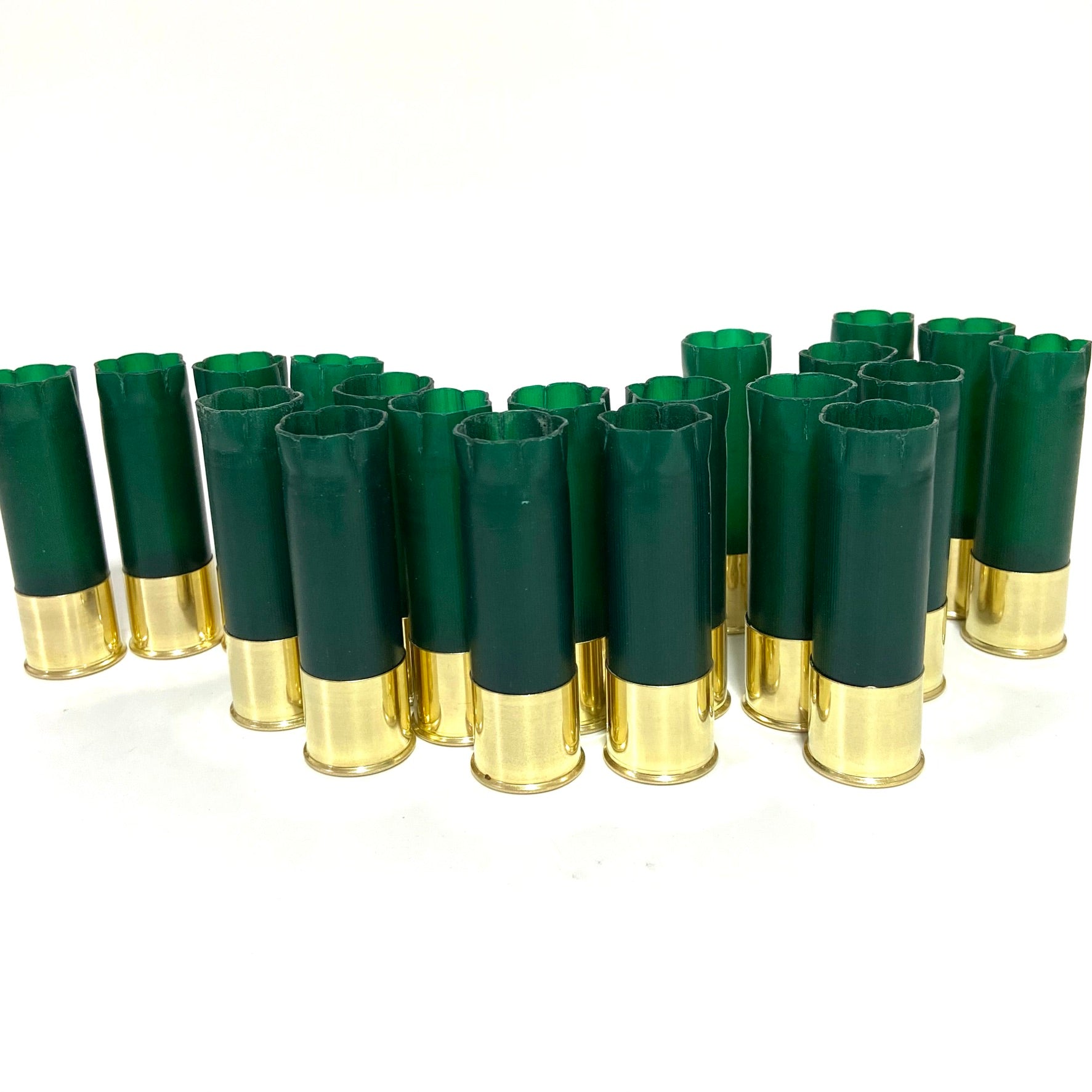 A large group of empty green shotgun shells with shiny brass bases standing upright on a white surface.