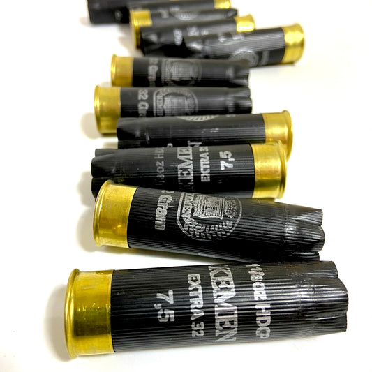 Row of black Kemen 12 gauge shotgun shells with brass bases, showing star-crimped tops and printed load markings
