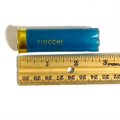 Light blue Fiocchi 12 gauge empty shotgun shell laid next to a wooden ruler showing a length of about 2.75 inches