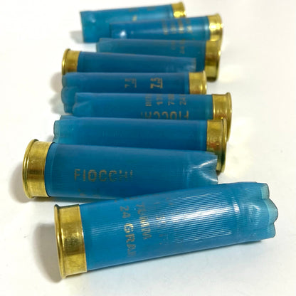 Row of light blue Fiocchi 12 gauge empty shotgun shells with gold bases lying on a white surface