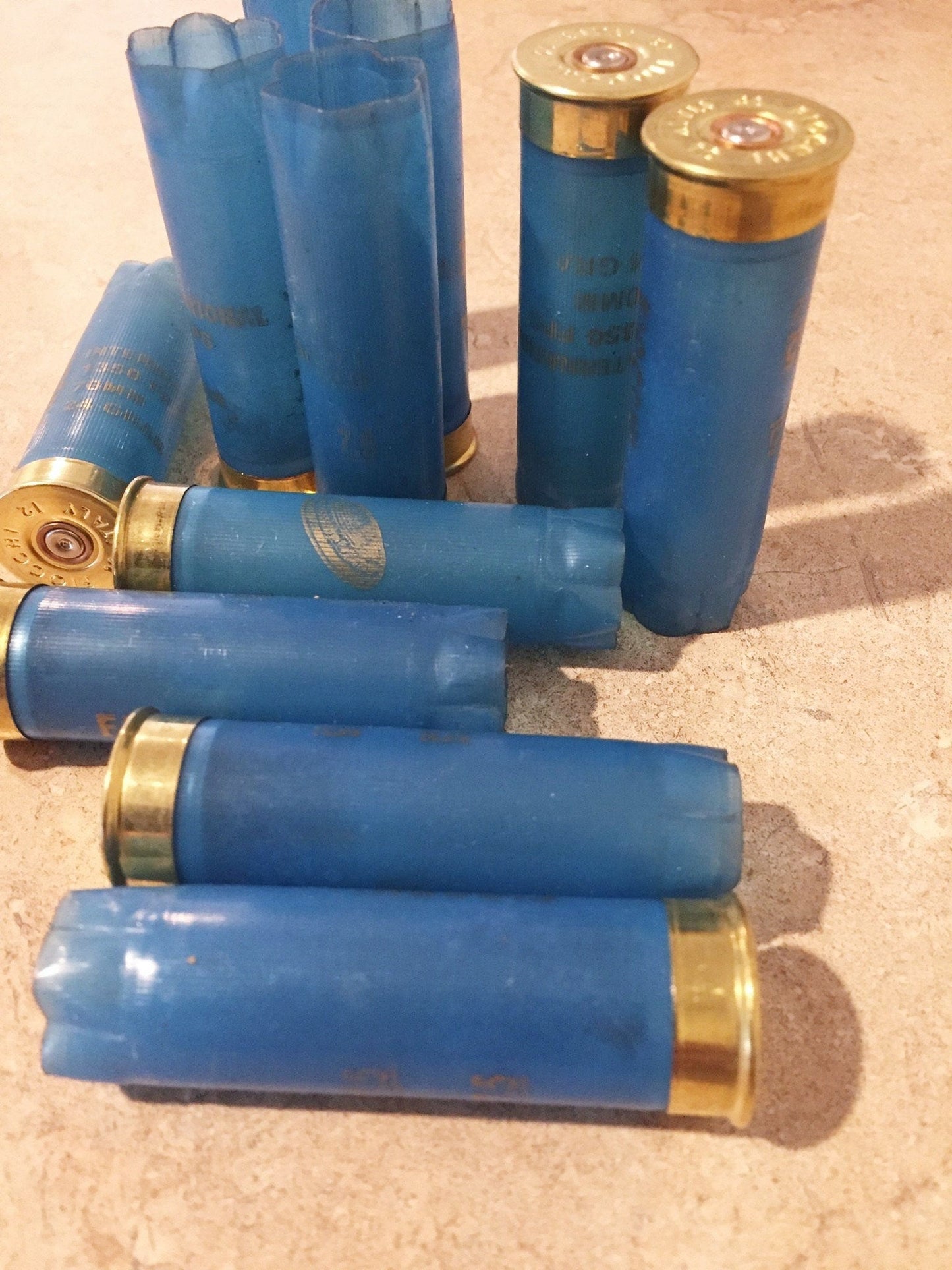 Light blue Fiocchi 12 gauge empty shotgun shells with gold bases scattered on a tan tabletop