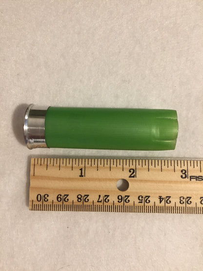 Single empty lime green 12 gauge shotgun shell with silver base next to a wooden ruler showing approximately 2.75 inches in length
