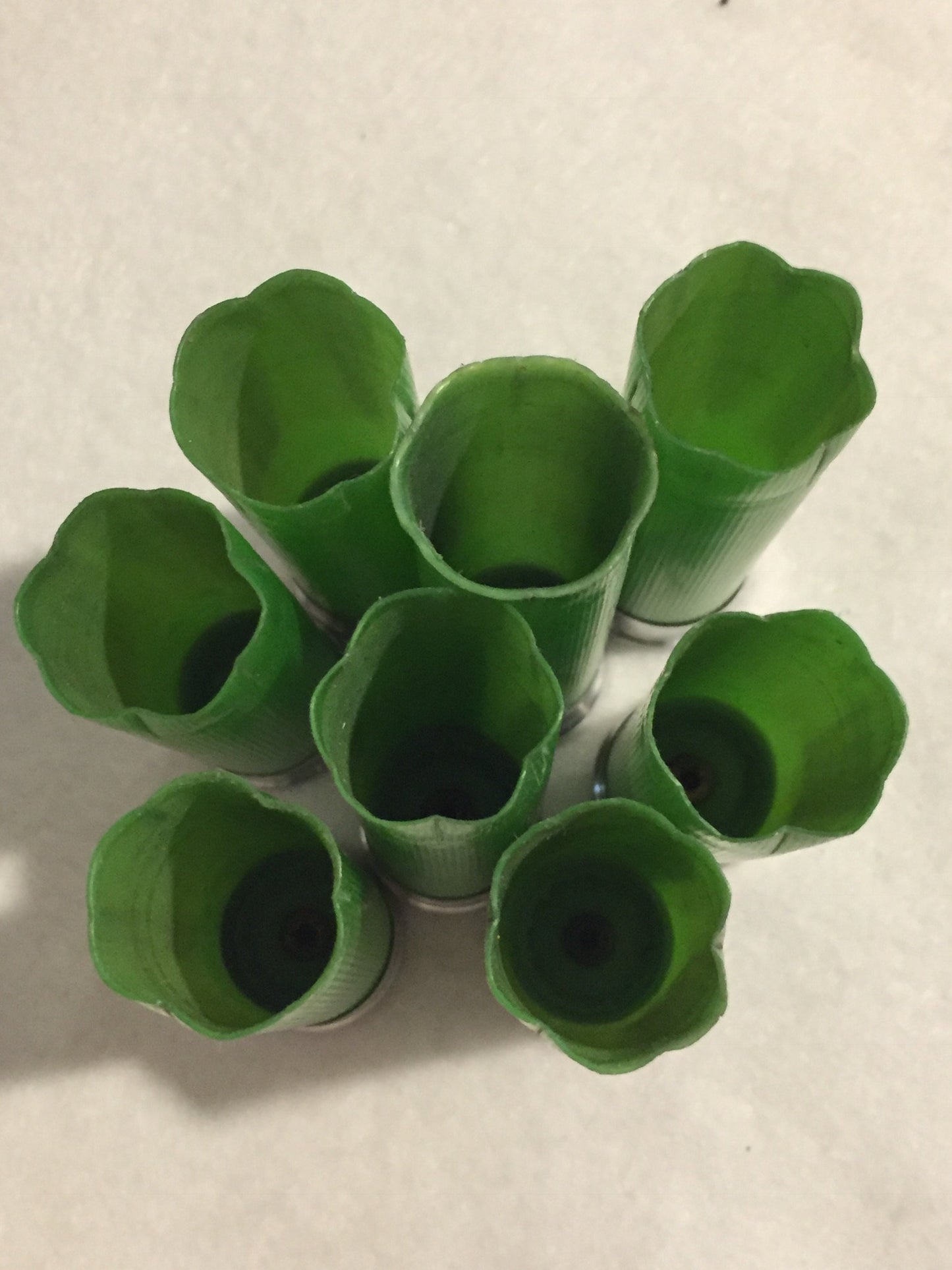 7 empty lime green 12 gauge shotgun shells with crimped open ends viewed from above showing hollow interiors