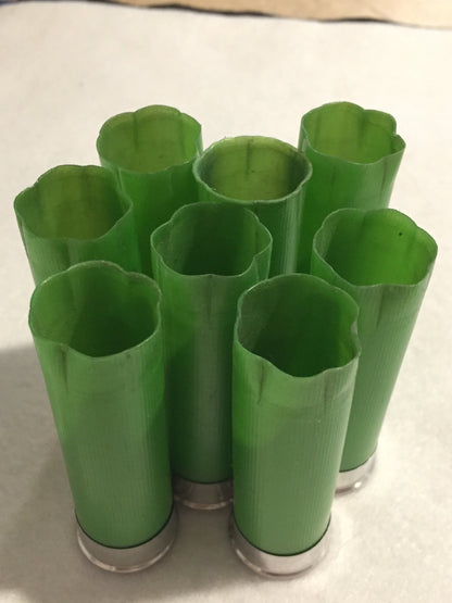 8 empty lime green 12 gauge shotgun shells with crimped open ends standing upright on a white surface