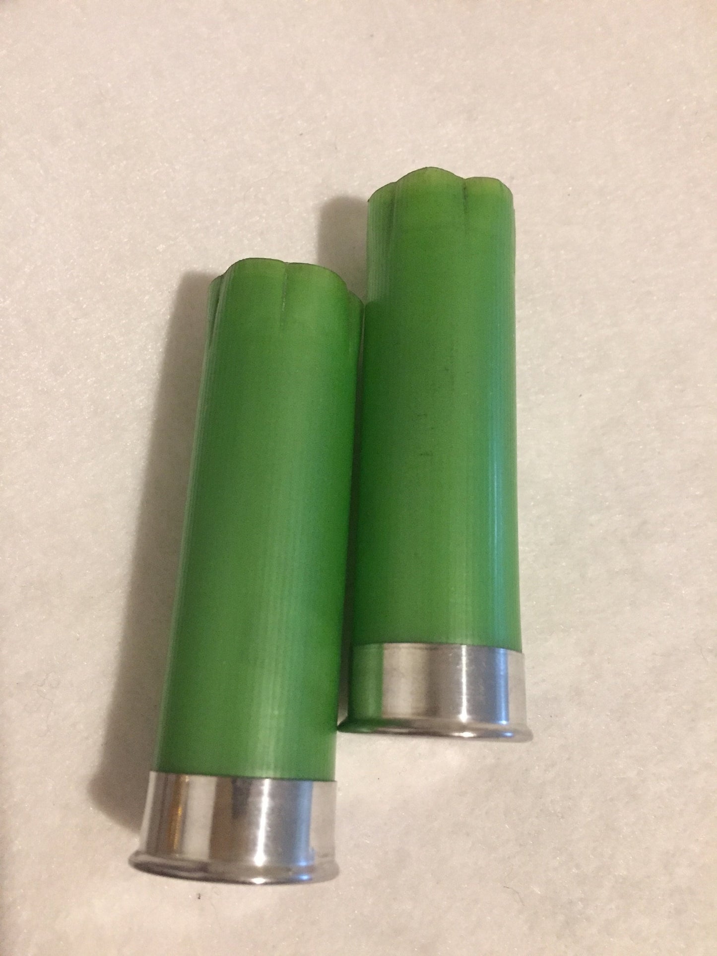 2 empty lime green 12 gauge shotgun shells with silver bases and crimped open ends on a white surface