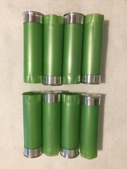 8 empty lime green 12 gauge shotgun shells with silver bases arranged in 2 rows on a white surface