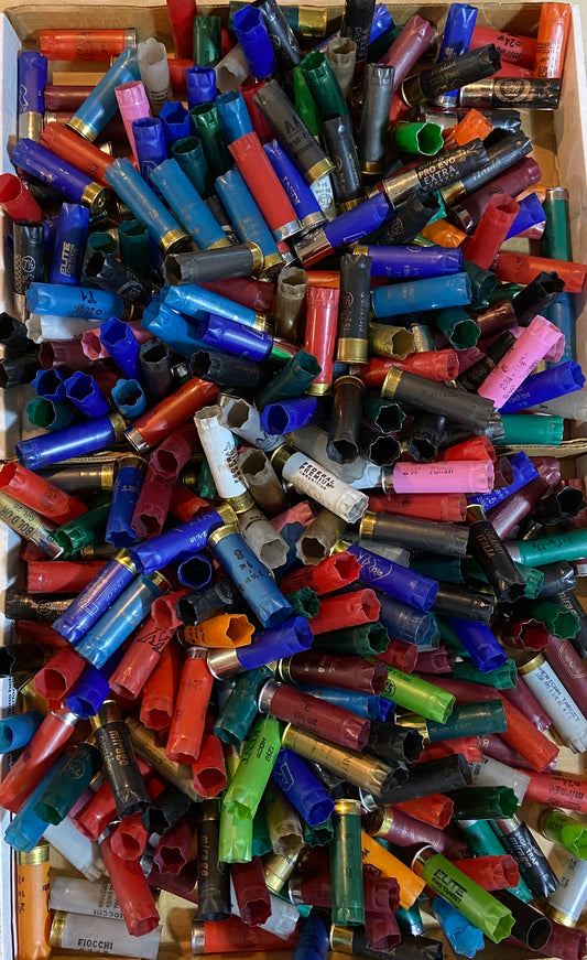 Top down view looking into a cardboard box filled with spent 12 gauge shotgun hulls in vibrant mixed colors bulk lot.