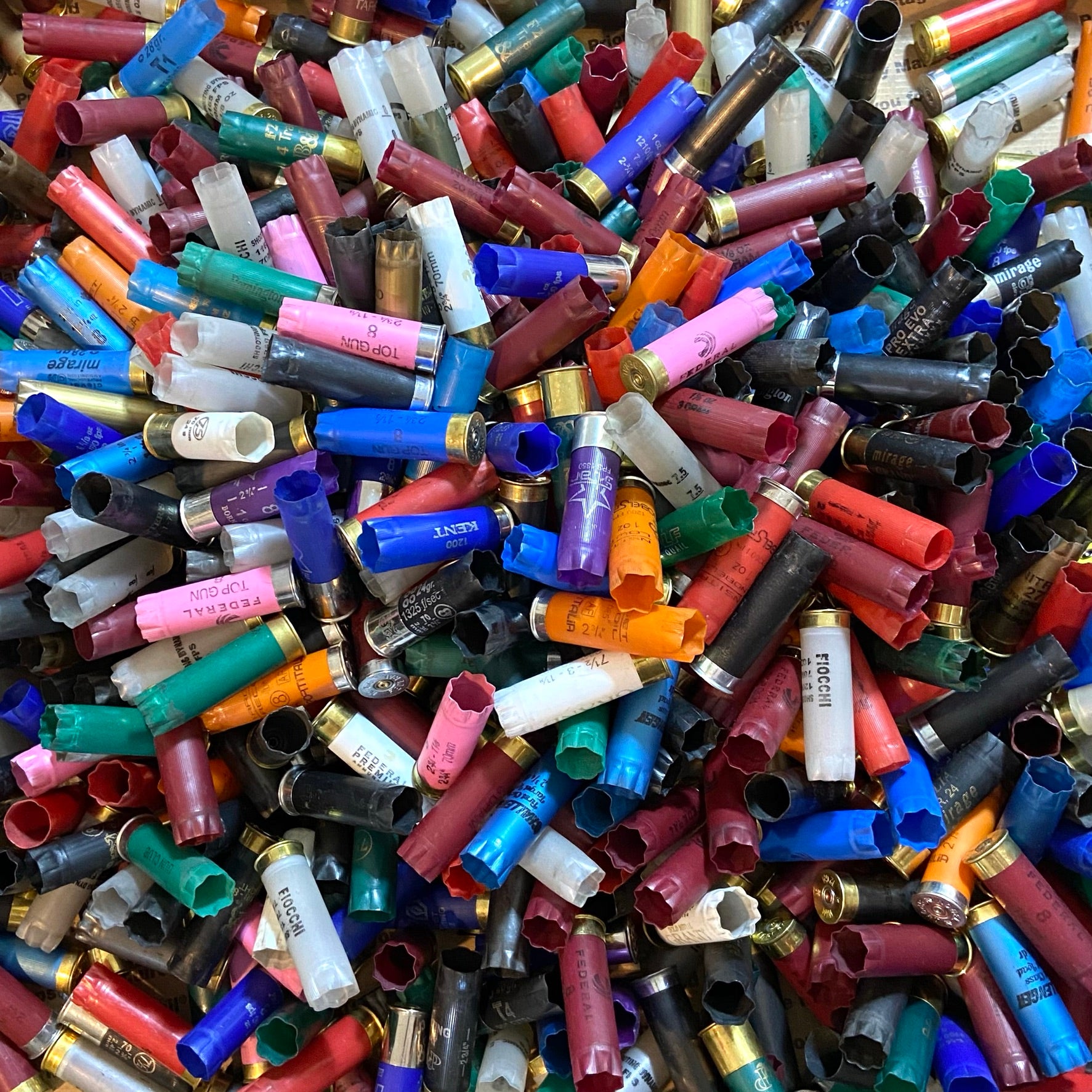Pile of mixed color 12ga shotgun hulls. Inert 12ga shells for crafts (no powder/spent primers).

