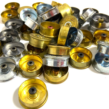 A pile of mixed gold and silver-colored 12 gauge shotgun shell cut bottoms.
