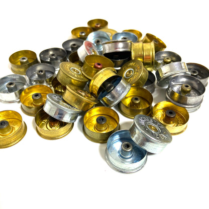 A close up of mixed gold and silver 12 gauge shotgun shell headstamps from various brands.
