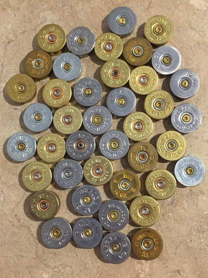 A collection of mixed gold and silver-toned shotgun shell bottoms from various brands on a textured surface.
