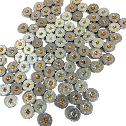 Silver 12 gauge shotgun shell bottoms scattered together on a white background, mixed brands.