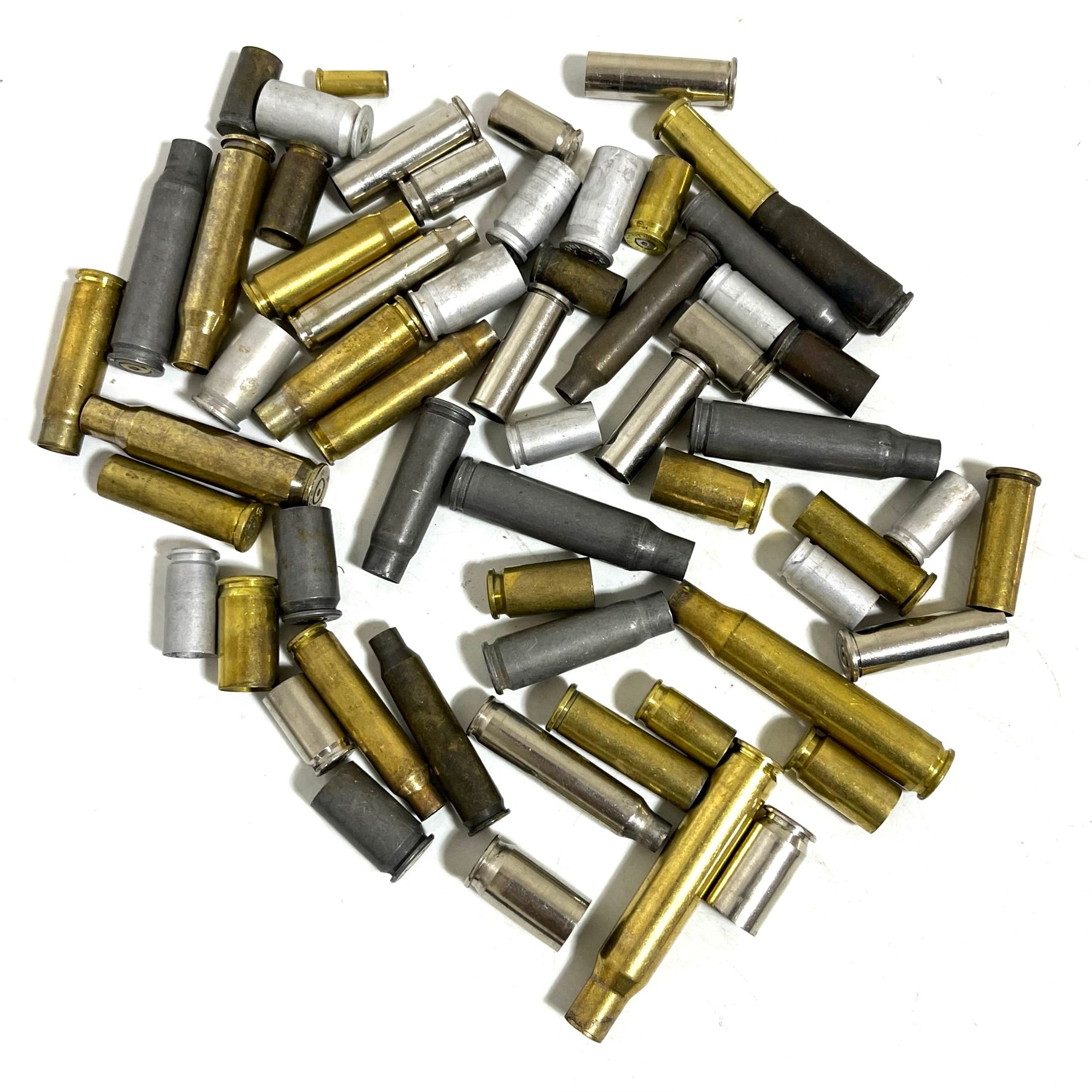 Dense pile of mixed spent bullet casings including rifle brass, dark steel, and silver nickel cases on a white background.
