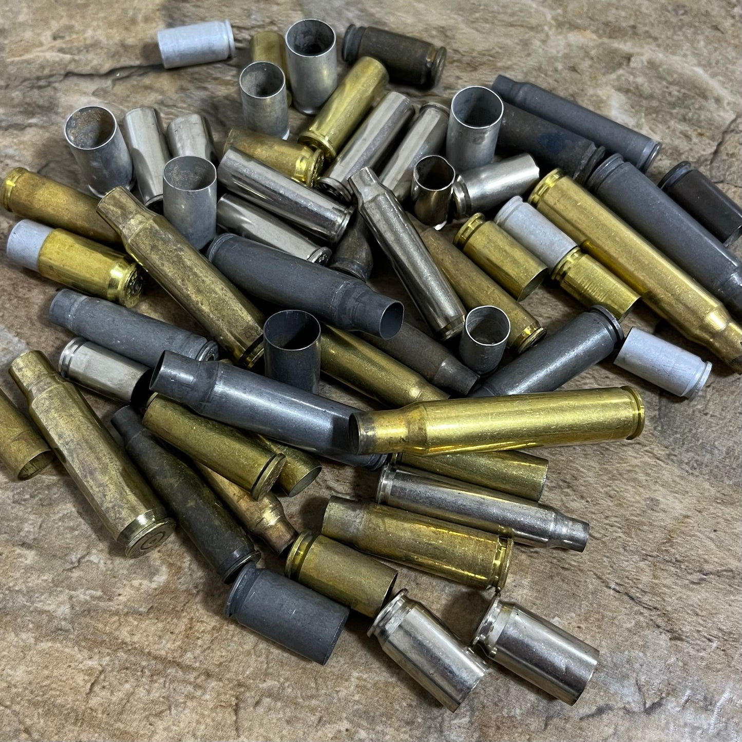 Pile of mixed spent bullet casings in brass, nickel, and steel displayed on a brown stone countertop.