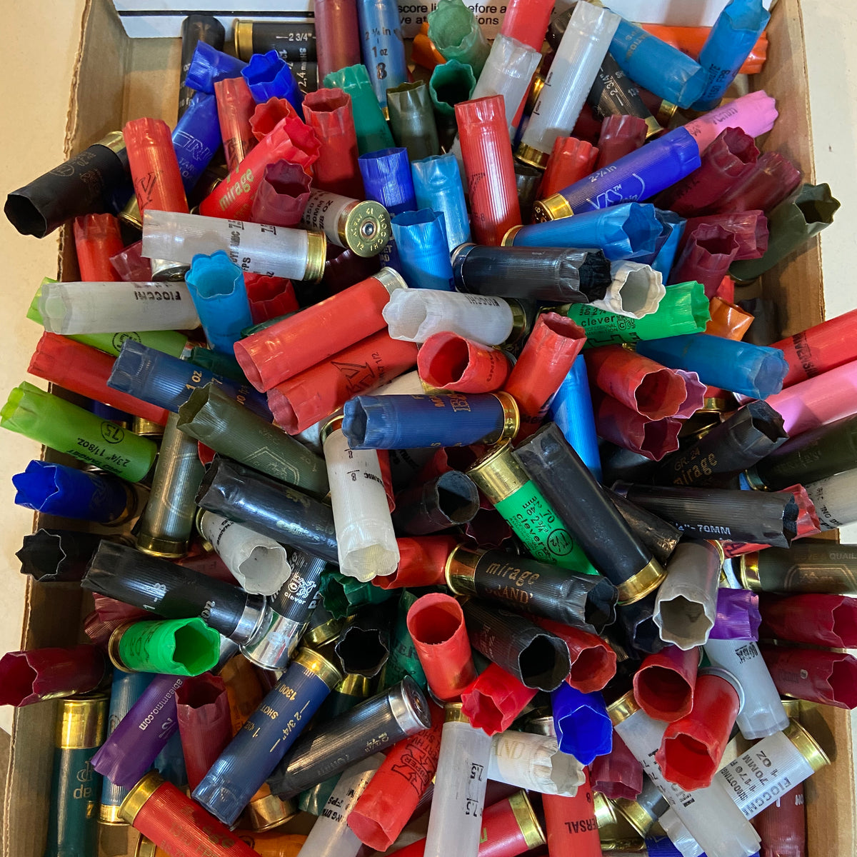 Mixed 12 gauge shotgun hulls in a box showing assorted colors, crimps, and headstamps