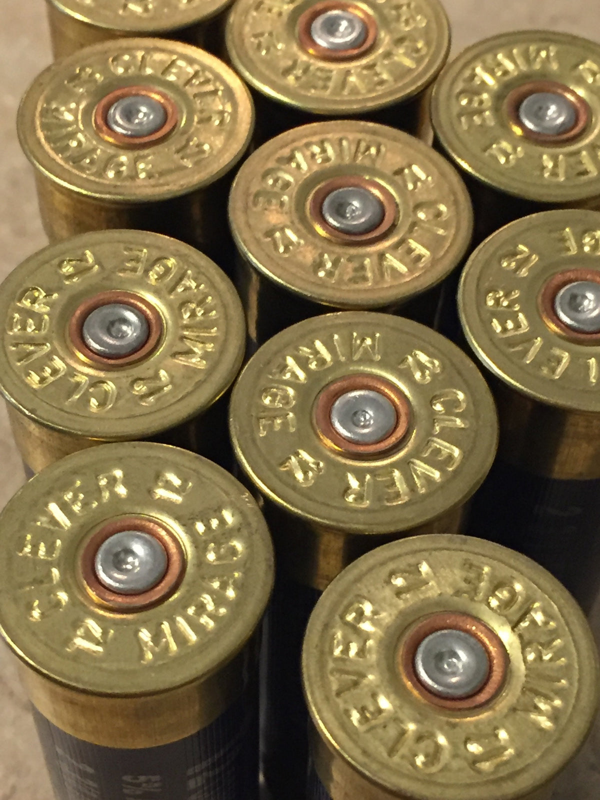 Close-up of navy blue shotgun shell brass headstamps reading Clever Mirage 12, gold primers with copper rings