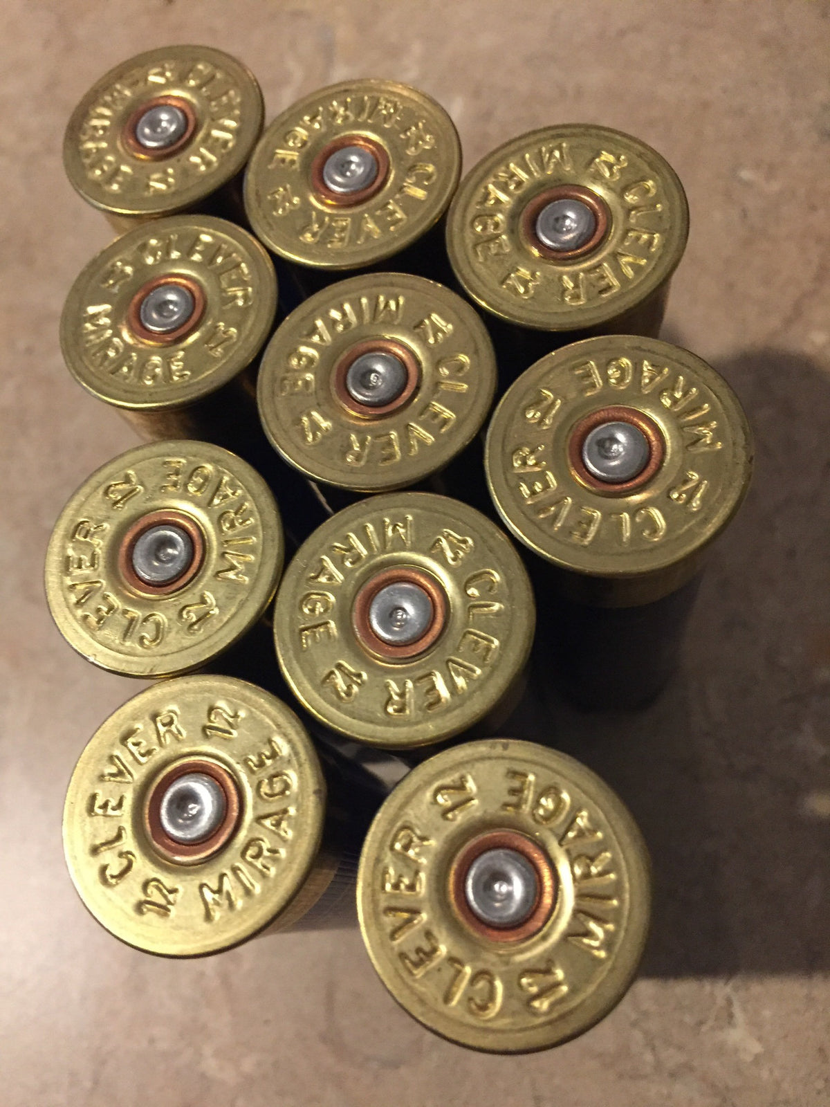 10 navy blue shotgun shell gold brass bases viewed from above, Clever Mirage 12 headstamps in cluster on tile