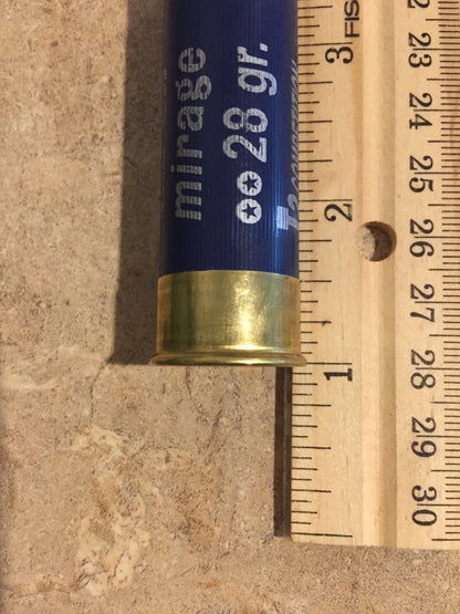 Single navy blue shotgun shell laid against a wooden ruler measuring approximately 2.7 inches from base to top