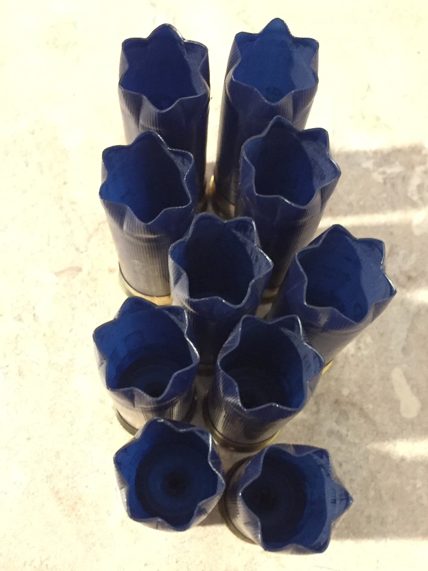 9 empty navy blue 12 gauge shotgun shells with crimped open ends viewed from above showing hollow interiors on a tile floor