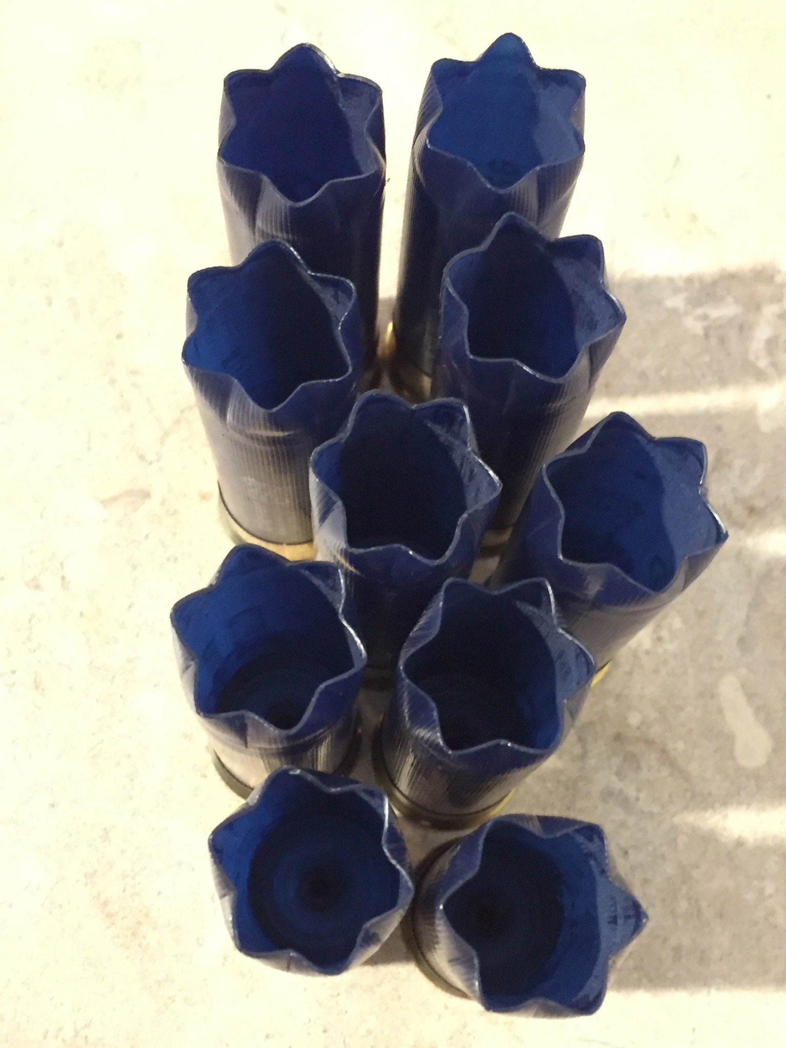 9 empty navy blue 12 gauge shotgun shells with crimped open ends viewed from above showing hollow interiors on a tile floor