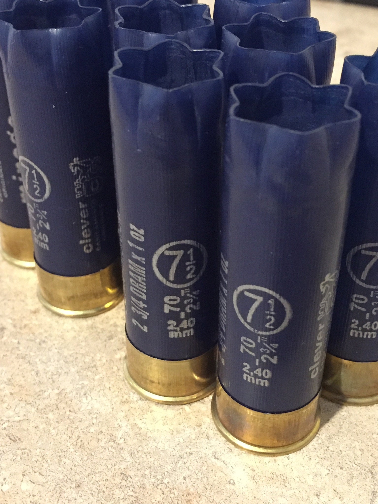 9 empty navy blue 12 gauge shotgun shells with crimped open ends standing on a stone surface
