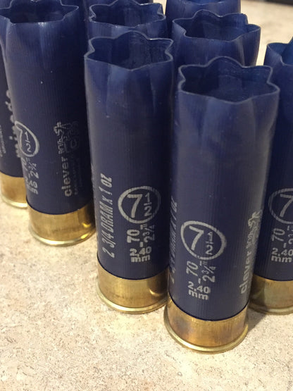9 empty navy blue 12 gauge shotgun shells with crimped open ends standing on a stone surface