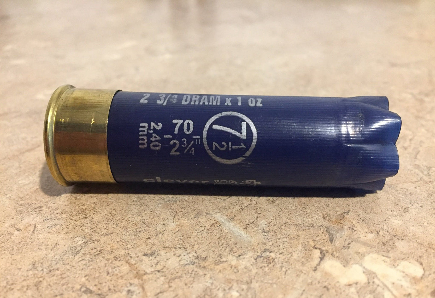 Single empty navy blue 12 gauge Clever Mirage shotgun shell with brass base on a stone surface