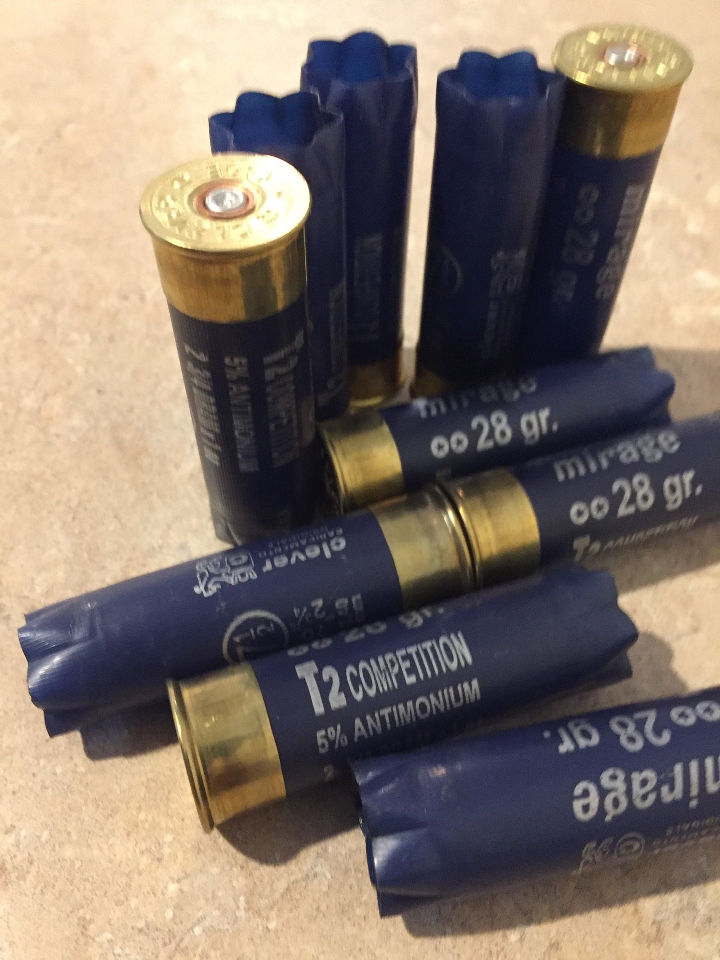 9 empty navy blue 12 gauge Clever Mirage and T2 Competition shotgun shells with brass bases arranged on a stone surface