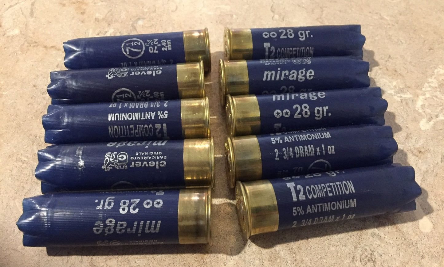 10 empty navy blue 12 gauge Clever Mirage and T2 Competition shotgun shells with brass bases on a stone surface