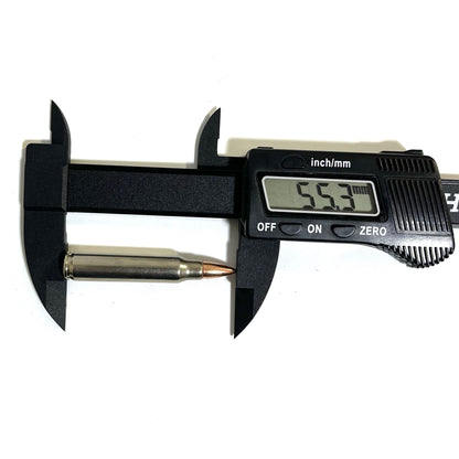 Black digital caliper measuring overall length of a nickel .223 dummy rifle cartridge showing 55.3 mm on display.