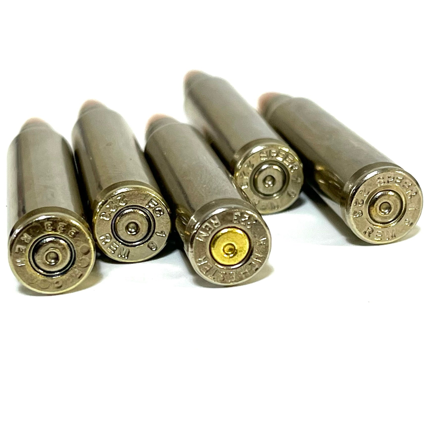 Five nickel-plated .223 dummy rifle cartridges angled toward camera showing stamped base headstamps and empty primer pockets.